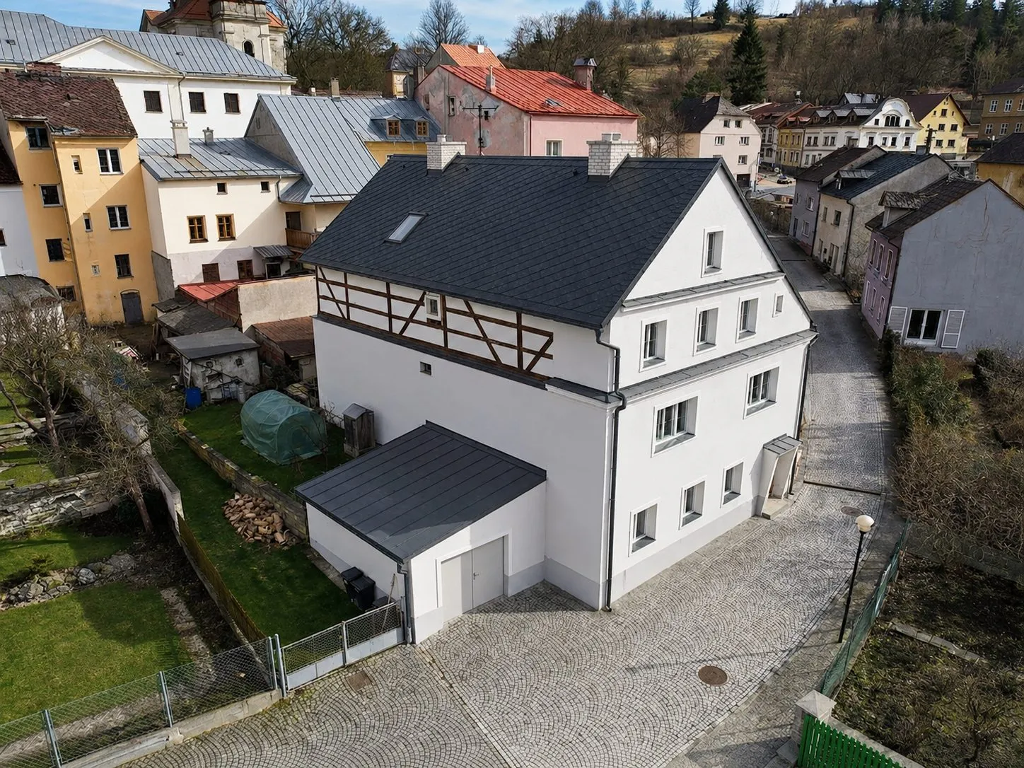 Letecký pohled na dům v Bečově — bílá omítaná hmota s hrázděným štítem a tmavou střechou, sevřená mezi historickou zástavbou městečka.
